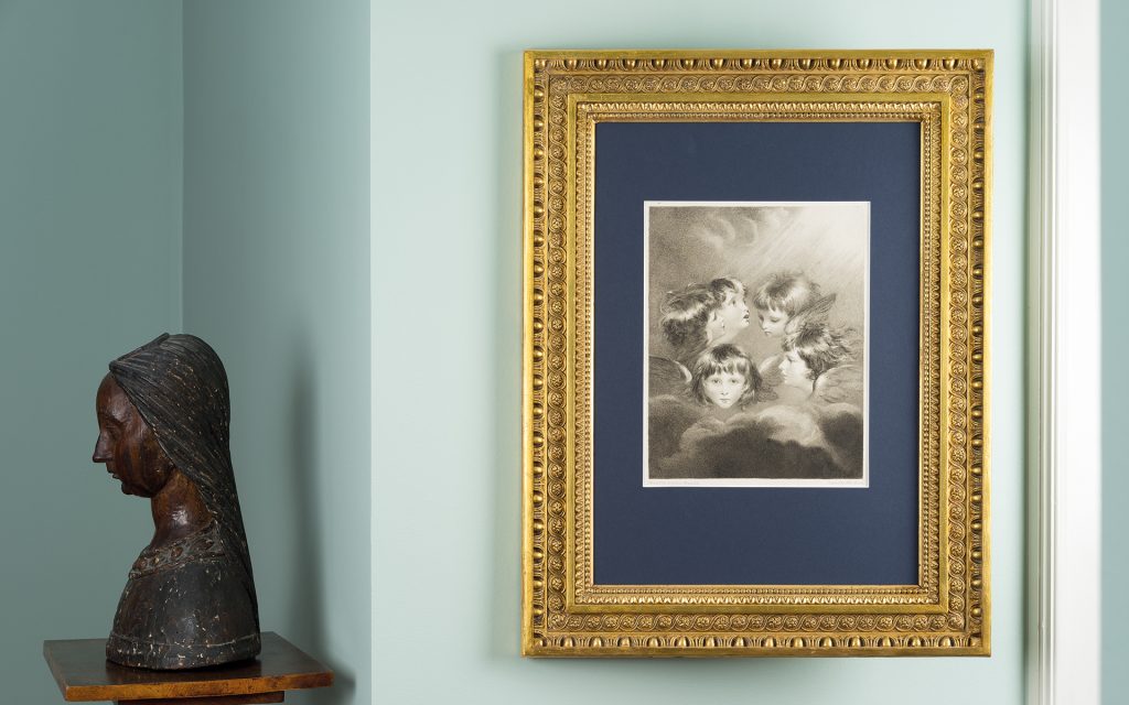 Gerahmtes Blatt mit blauem Passepartout neben einer Madonnenskulptur aus Holz